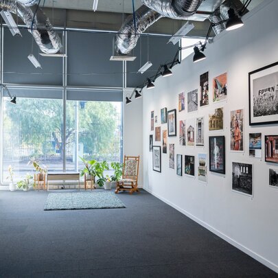 Interior gallery space with white walls densely hung with various framed photos and artworks.