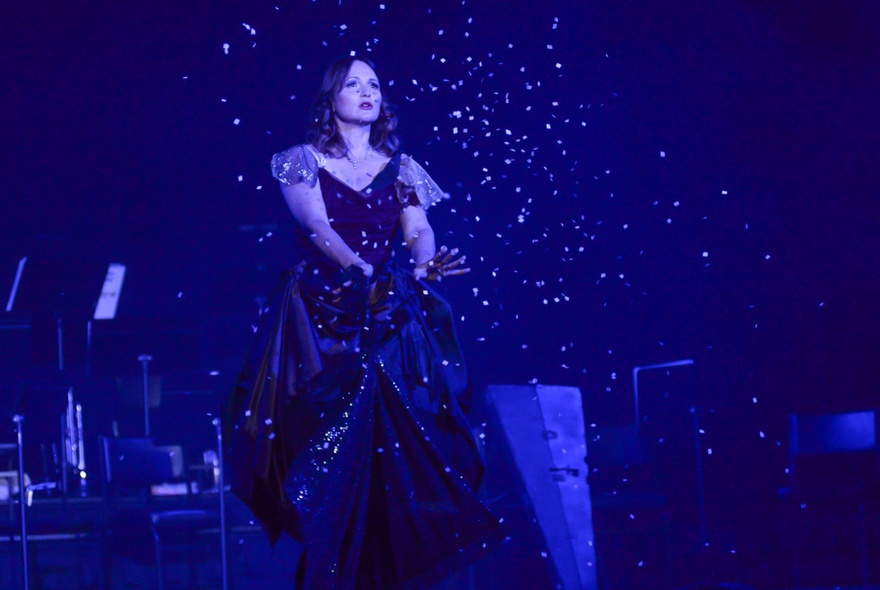 A performer on stage amongst twinking lights wearing a black ball gown.