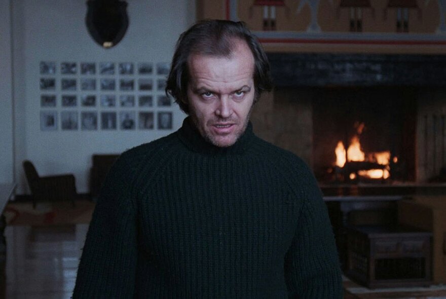 Film still from The Shining, Jack Nicholson glowering in front of a fireplace.