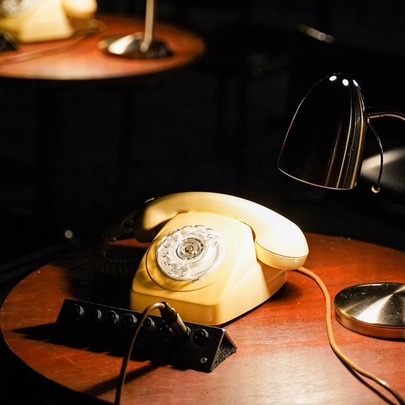 A yellow vintage phone on a wooden table illuminated by a desk lamp, part of an interactive theatre installation at the Malthouse Theatre.