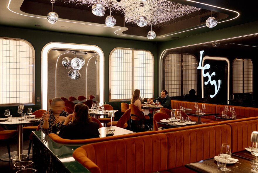 A chic dining room with orange booth seating and glass orbs hanging from the ceiling.