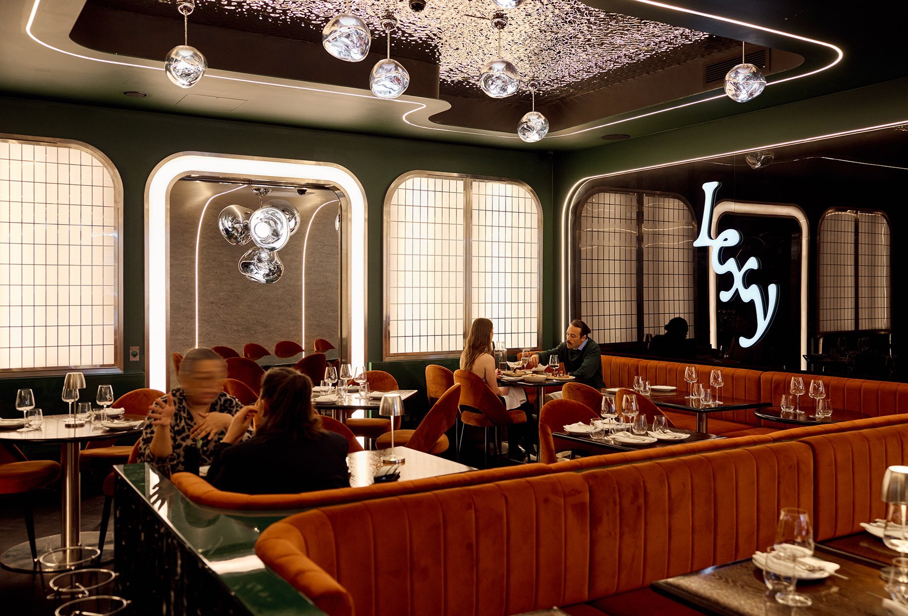 A chic dining room with orange booth seating and glass orbs hanging from the ceiling.