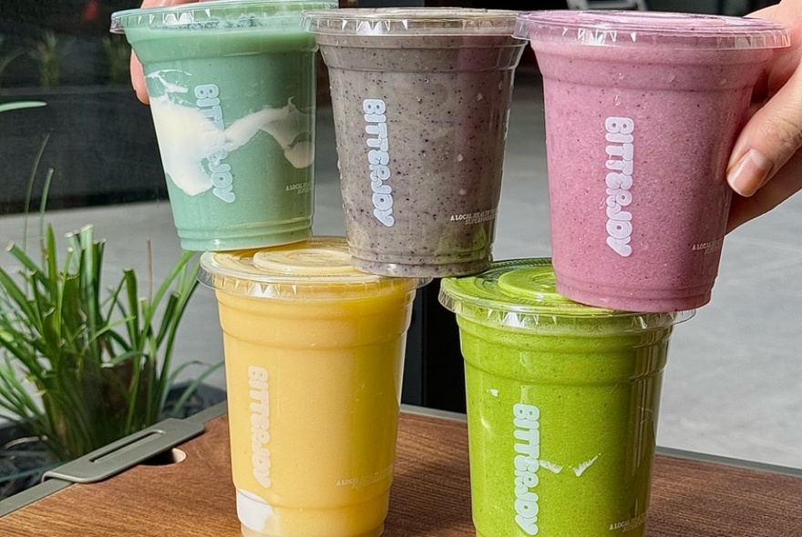 Five different Bitterjoy smoothies in clear cups displayed on a table.