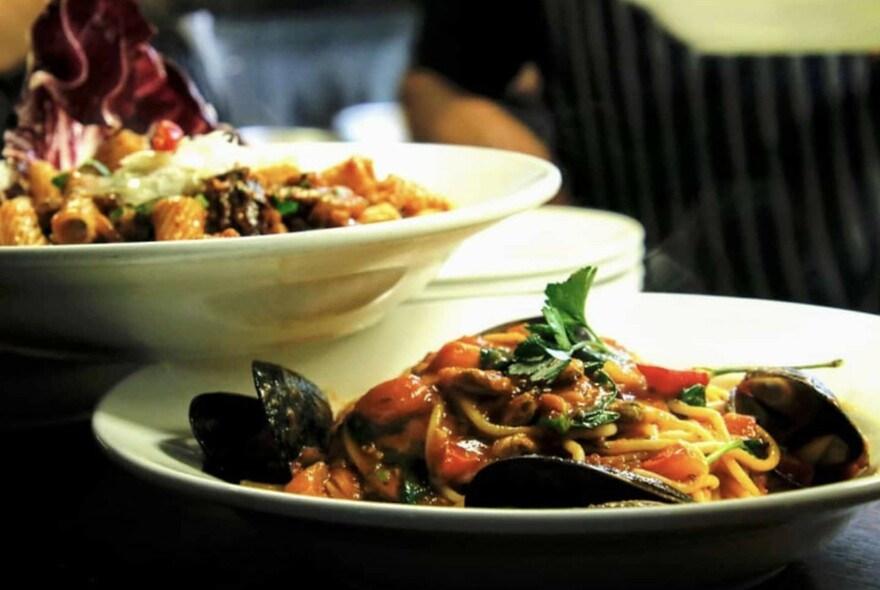 A bowl of pasta rested of top of a bowl of spaghetti and mussels.