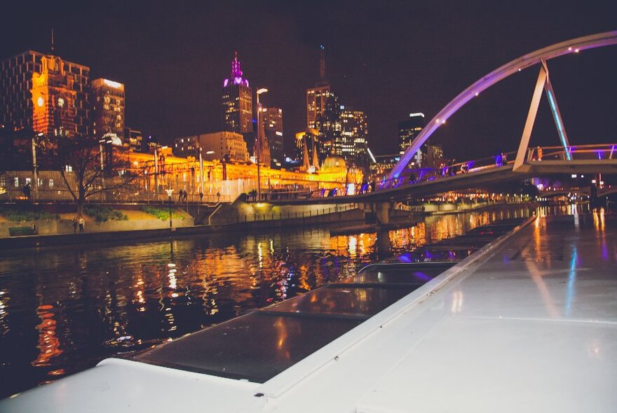 View of the Melbourne skyline from a cruise at night with coloured lights on show. 