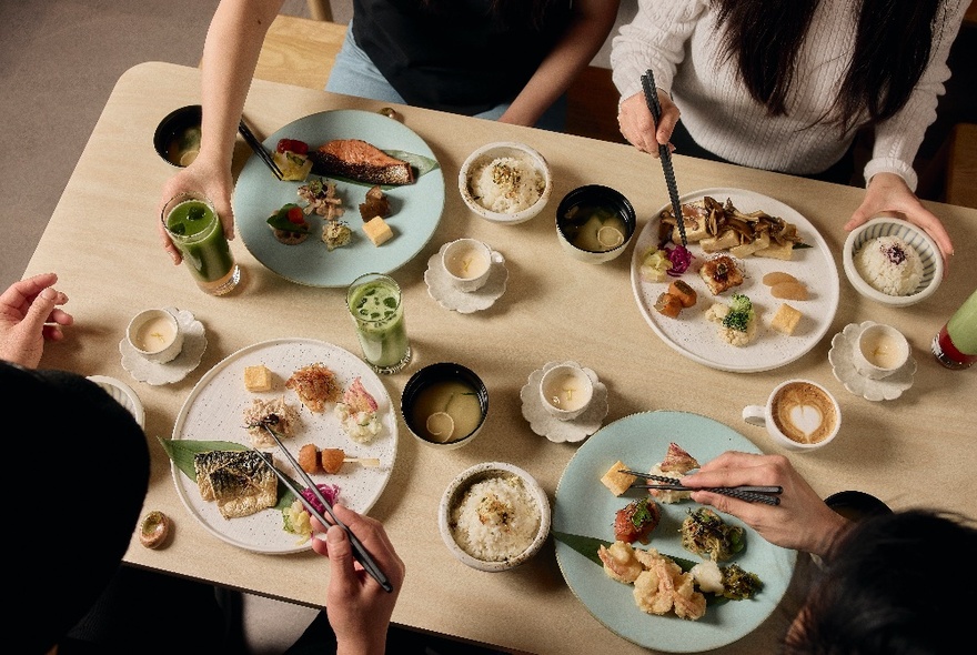 Overhead view of a table filled with dishes of Japanese food and people seated at bench seats eating and drinking.