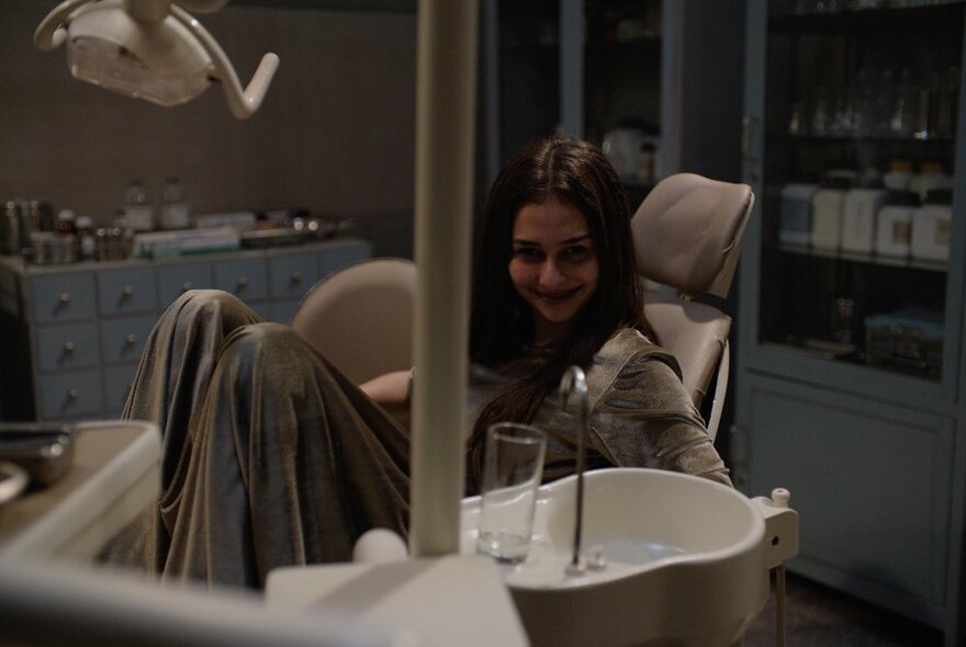 A young woman leaning back in a chair in a dimly lit dentist's clinic.