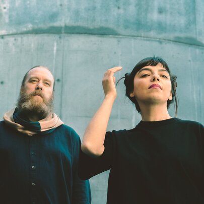 Two members of the music group ZÖJ both posing looking in the distance against a concrete building. 