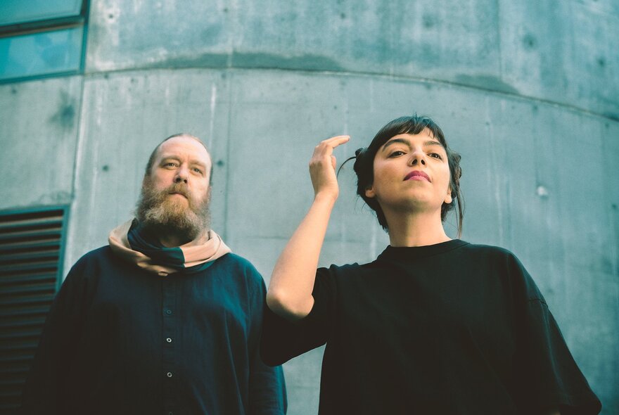 Two members of the music group ZÖJ both posing looking in the distance against a concrete building. 