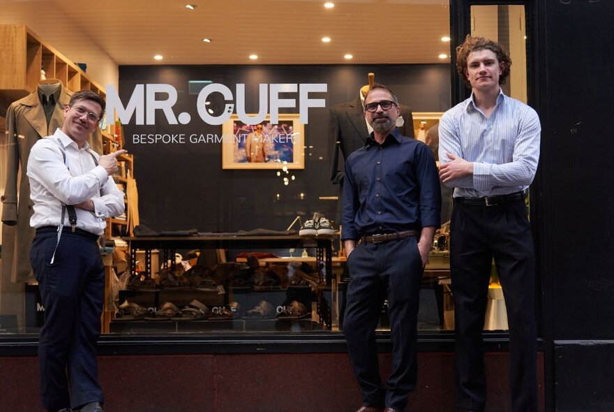 Three men standing outside the large window of the retail shop Mr Cuff, looking directly at the viewer.