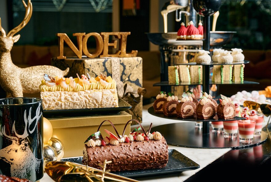 A Christmas buffet with yule log, small cakes, trifle cups and a sign saying NOEL. 