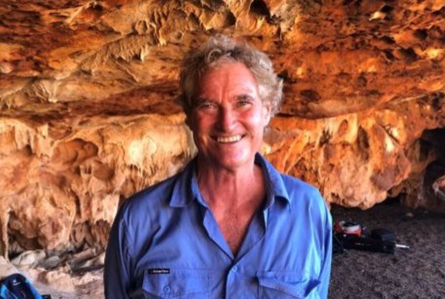 Archaeologist Peter Veth smiling while standing in front of a rock shelter.