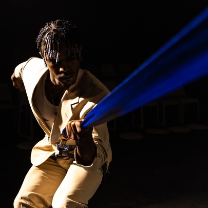 Dancer wearing a beige suit, holding a blue strap.