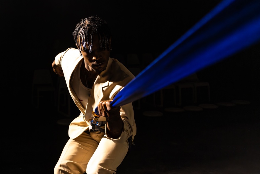 Dancer wearing a beige suit, holding a blue strap.