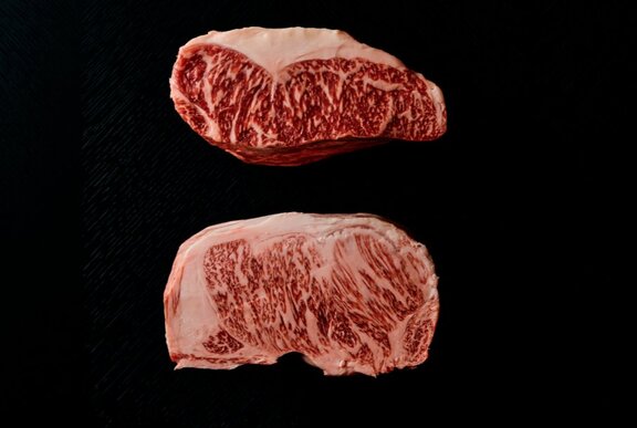 Slabs of raw marbled Wagyhu beef on a black background.