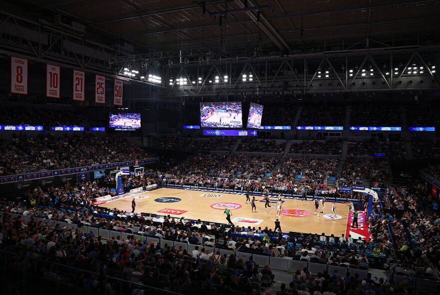 A National Basketball League match underway inside John Cain Arena at Melbourne Park, with an indoor court and spectators watching from the stadium seats.