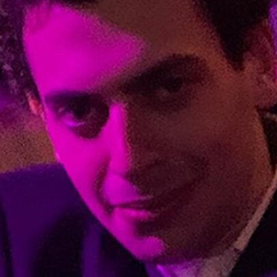Close up amd slightly pixellated photograph of Comedian Jake Zukerman with a pink light shining on his face.