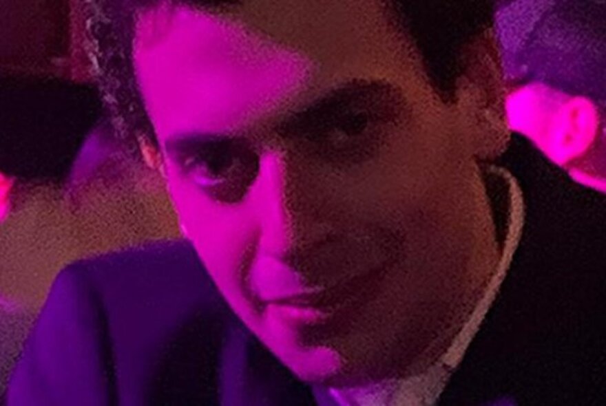 Close up amd slightly pixellated photograph of Comedian Jake Zukerman with a pink light shining on his face.