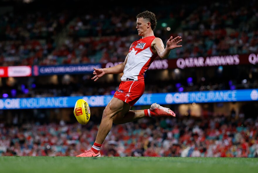 A Sydney Swans footballs mid-kick in front of a crowd. 