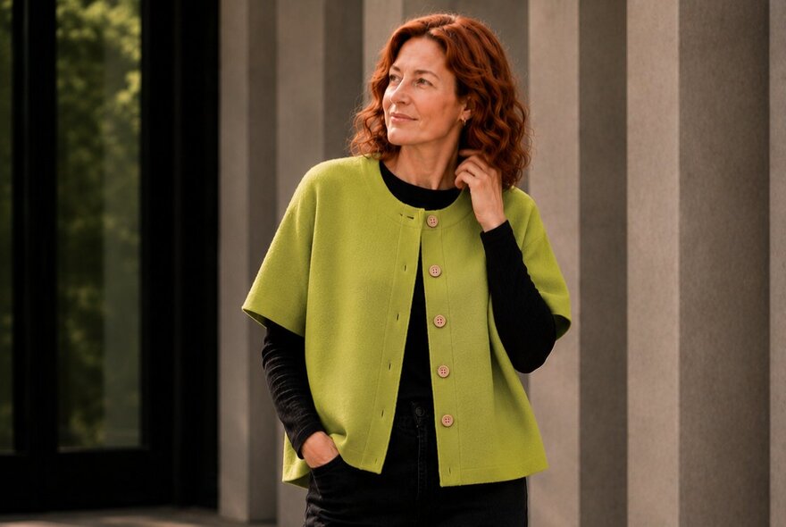 Model wearing a loose short-sleeved lime green button-up top over a long-sleeved black top.