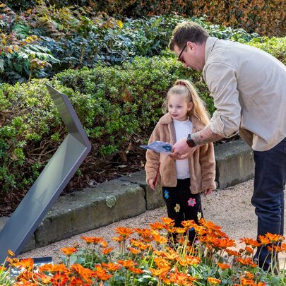Adult and child looking at a pamphlet in a garden.