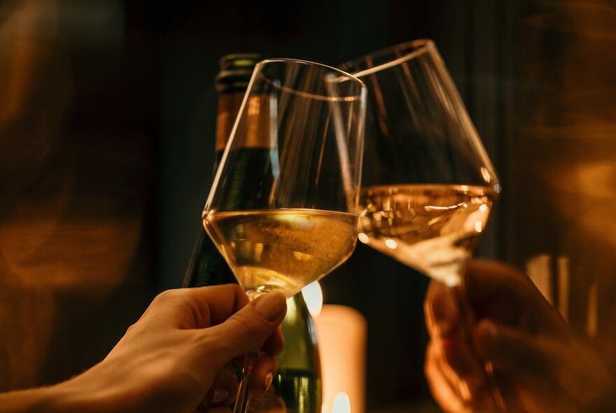 Two glasses of white wine with the light shining through them, a bottle behind.