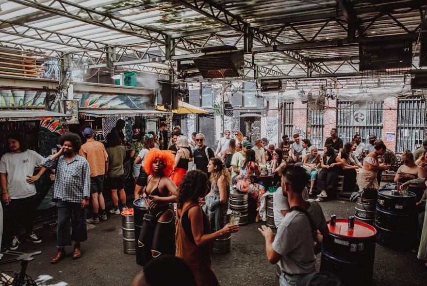 Patrons at Section 8, a shipping container bar in Melbourne with industrial decor and barrels as tables.