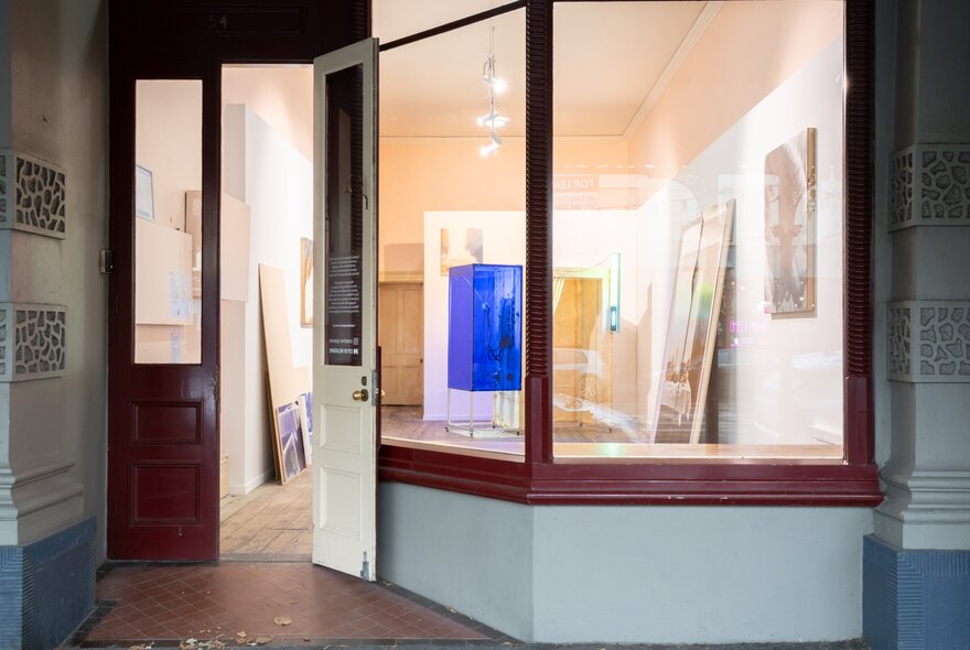 The exterior of Blindside Gallery, with an open door, and a large window showing the white walls and artwork inside. 