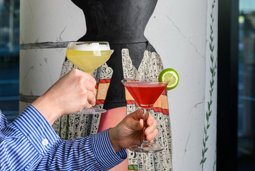 A pair of hands holding two different cocktails.