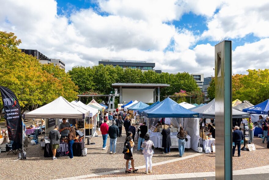 An outdoor market in a park with tented stalls. 