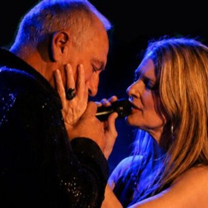 A male and female singer caressing each other's faces as they sing together on stage.