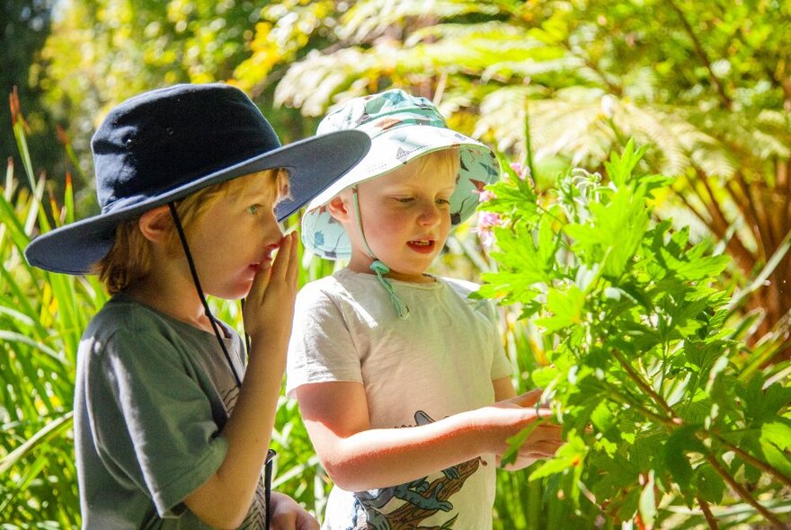 Young children playing outdoors in a garden and interacting with foliage.