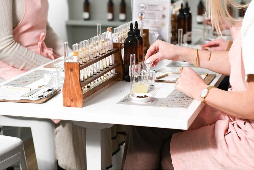 Two people seated at a workstation in front of oils and fragrances in vials during a perfume-making workshop.