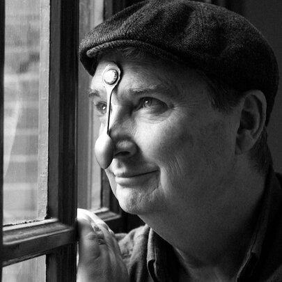 Man peering through a window, wearing a cap with a spoon resting on his nose.