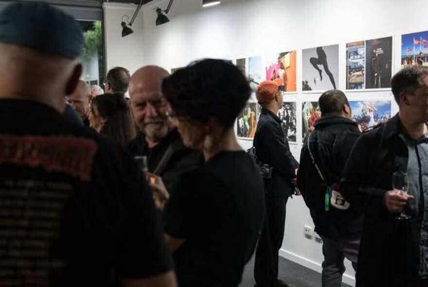 People socialising and viewing artworks on the wall in a gallery setting.