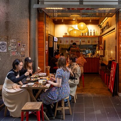 View from the street into a small and cosy interior of a cafe, a table of diners on the footpath and people also dining inside the small cafe.