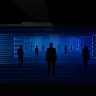 A light show experience with people walking through a darkened space with a deep blue light illuminating them. 
