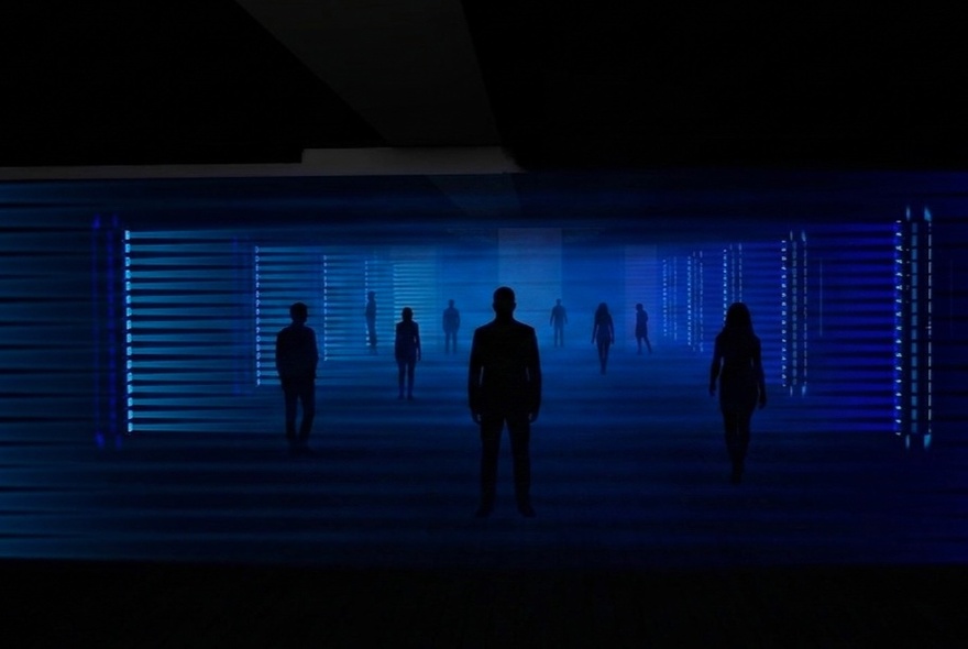 A light show experience with people walking through a darkened space with a deep blue light illuminating them. 