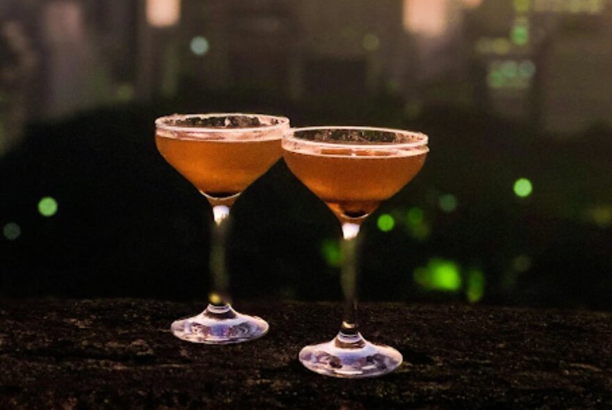Two pink cocktail glasses on a dark bench.