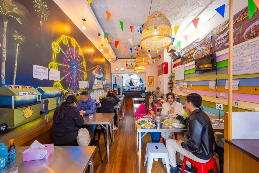 People dining in a colourful restaurant with flags and a mural.