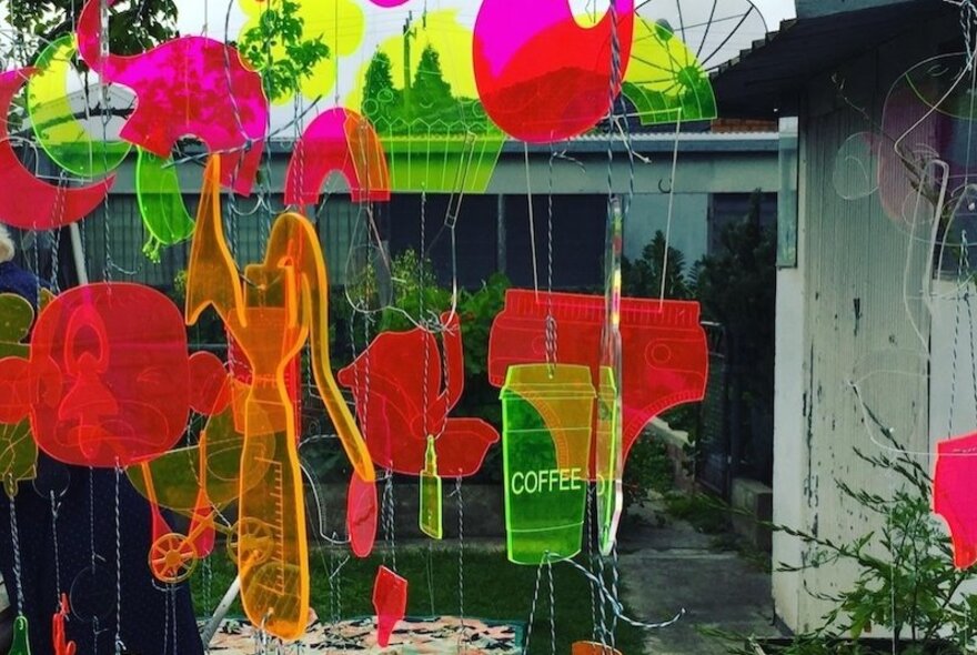 Colorful hard plastic suncatchers, including a flamingo shape and one shaped as a disposable cup with the word COFFEE written on it, hanging outdoors.