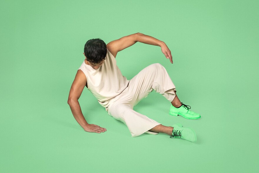 A person demonstrating a dynamic dance move while wearing a comfortable, neutral-toned sleeveless top and trousers, set against a green background.