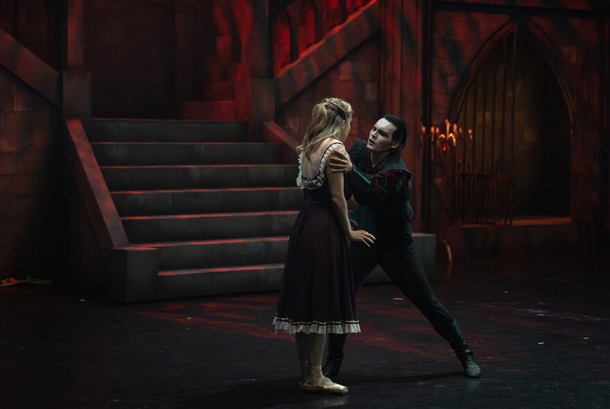 A young woman standing near a dark staircase next to a gothic white-faced Dracula figure.