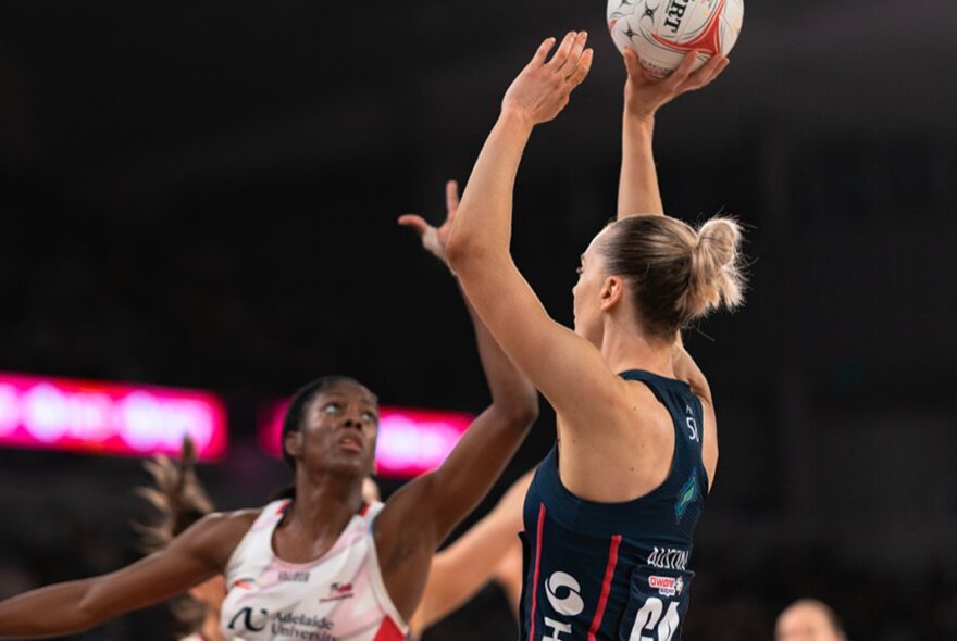A Melbourne Vixens netballer holds the ball above her head as she prepares to take a shot at goal.