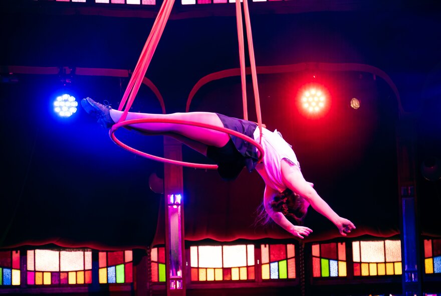 An acrobat swinging from ropes and a hoop under two red and blue spotlights. 