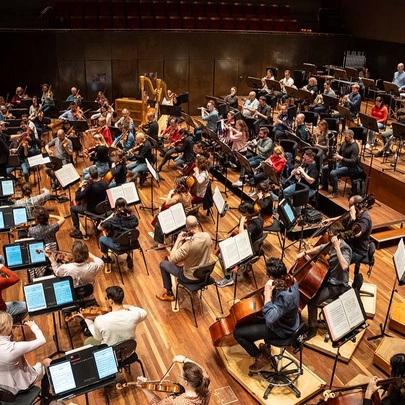 Looking down through a distorted lens at an orchestra in plain clothers playing in an auditorium.