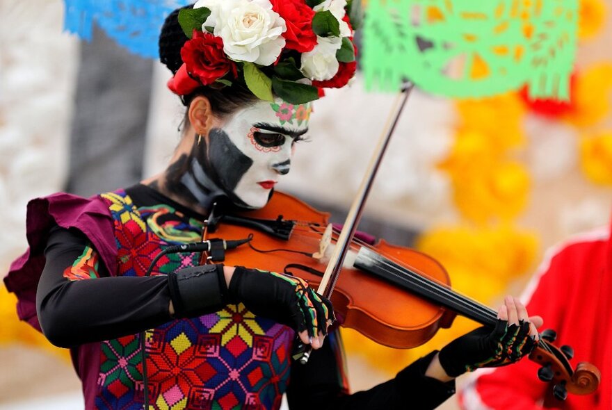 A musician playing the viola dressed in a Day of the Dead costume, face paint and a floral headpiece.