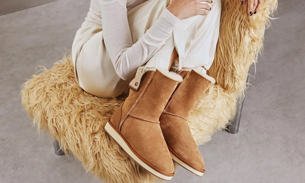 A model in brown ugg boots curled up in a chair with a furry throw.