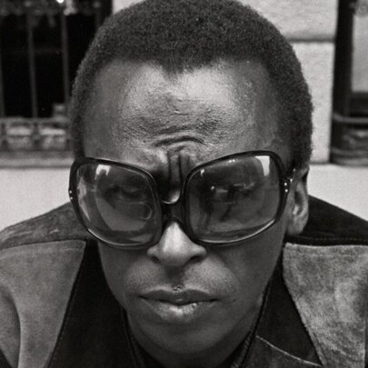 Miles Davis wearing oversized sunglasses and suede jacket.