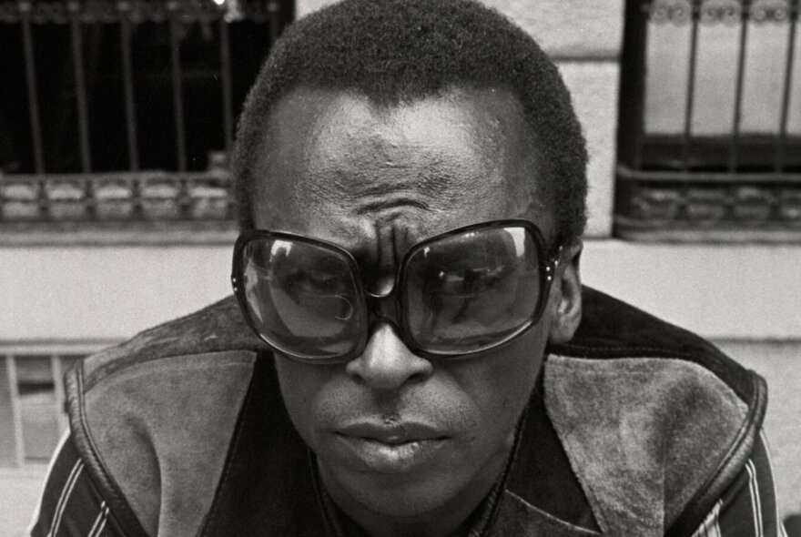 Miles Davis wearing oversized sunglasses and suede jacket.